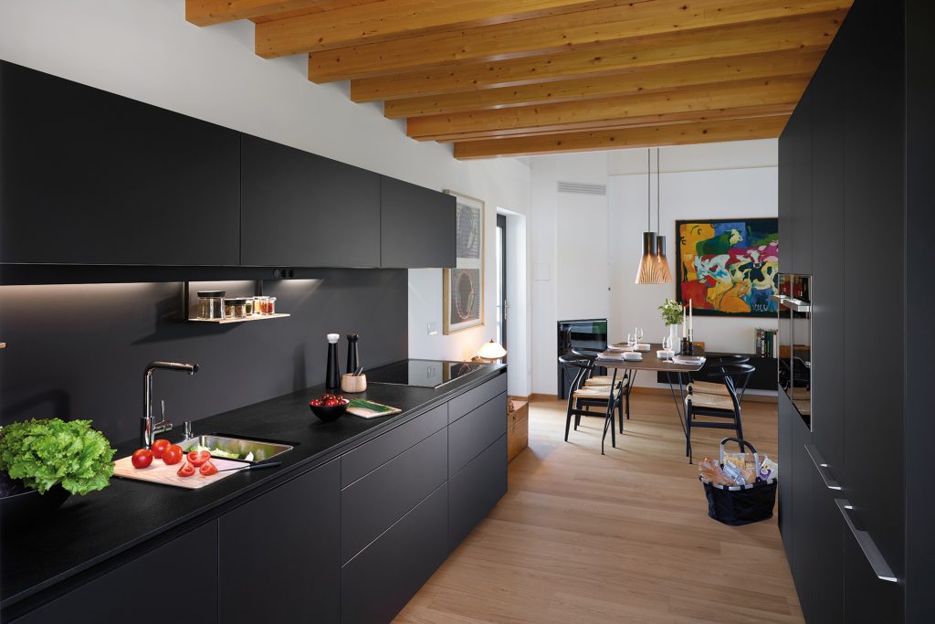 Black parallel kitchen that opens into the dining room, fitted with cabinets designed by Santos