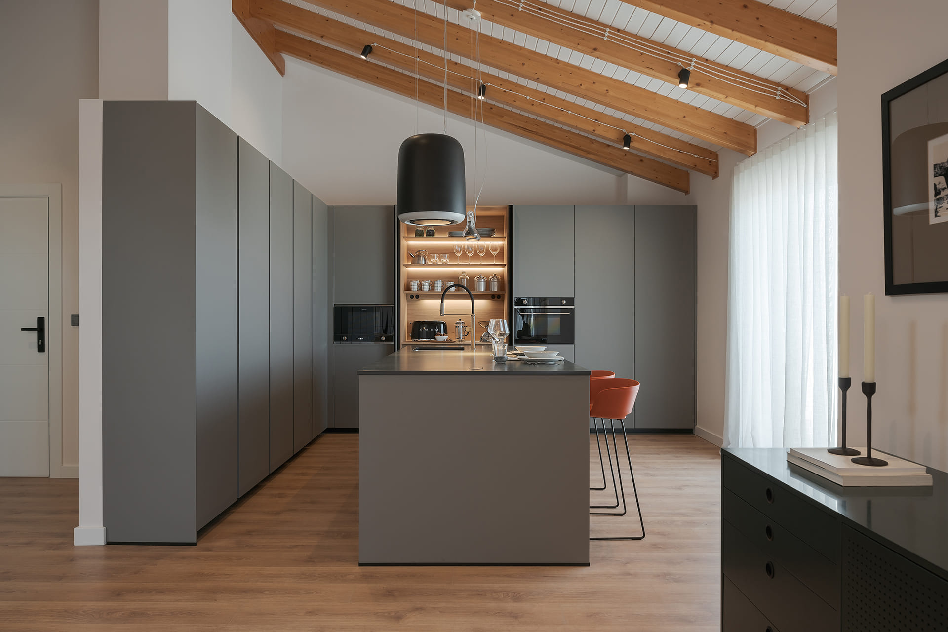 Grijze keuken met eiland en houten vloeren, open ontwerp naar de zitkamer.