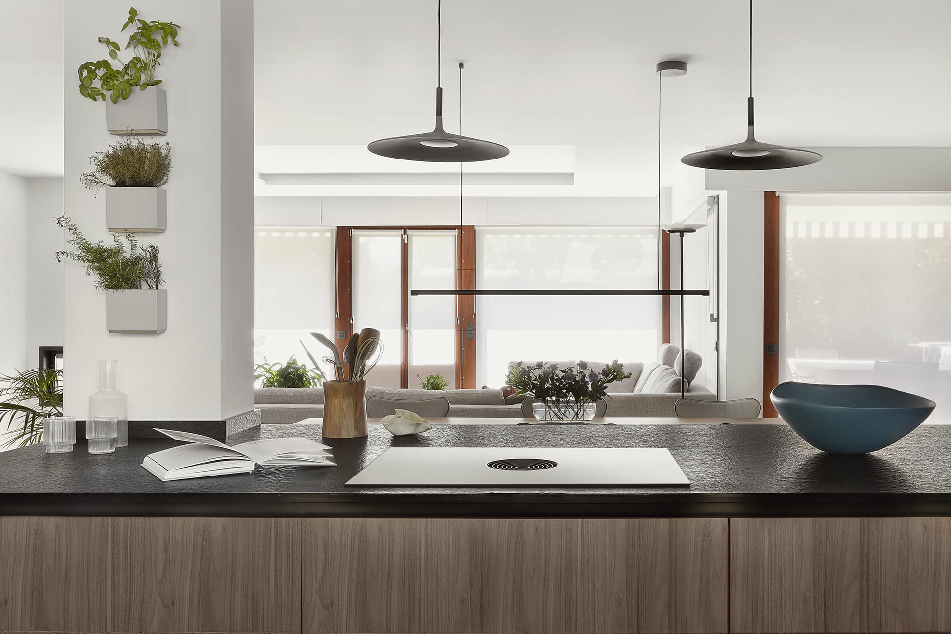 Grey kitchen with island, black worktop and walnut wood cladding.